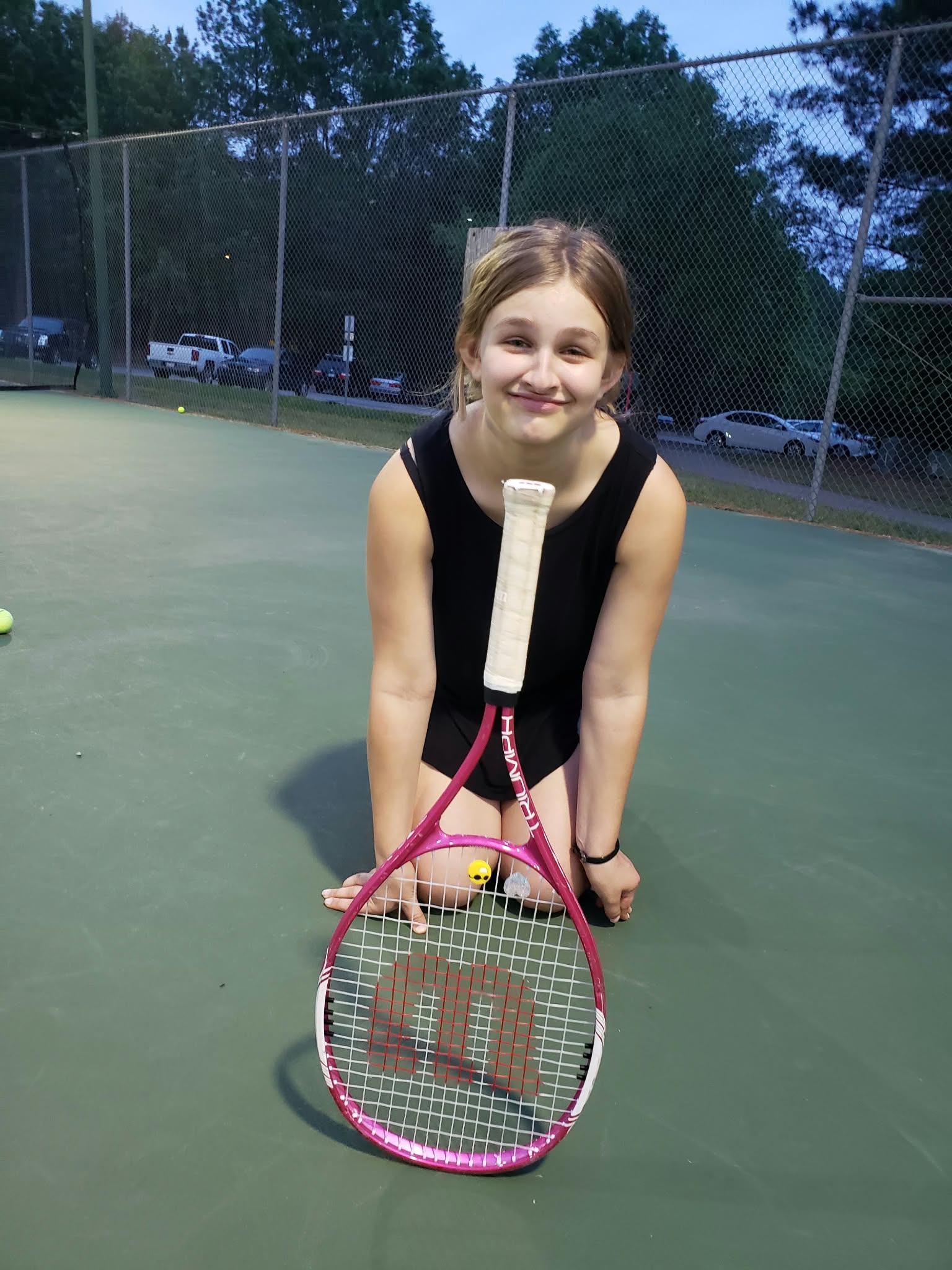 Young tennis student smiling with her racket on court